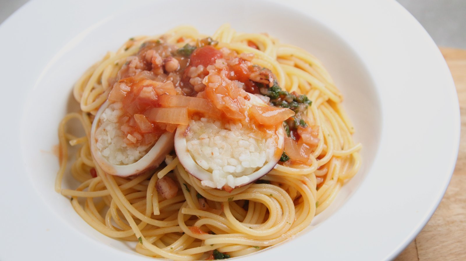 トマトソースをかけたスルメイカの洋風イカ飯を輪切りにし、パスタにのせた一皿